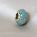 Gold bead, teal shimmer, lightly ashes, subtle silver flecks